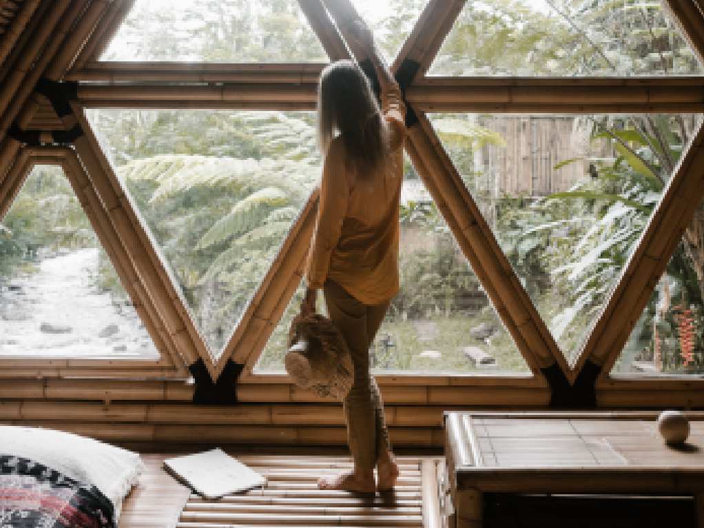 Woman by triangular bamboo-framed windows overlooking a jungle